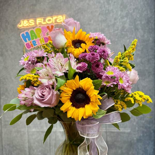 Mixed bouquet with sunflowers, pink roses, and purple blooms in a glass vase