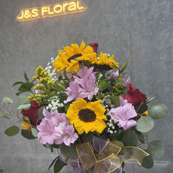 Bouquet of sunflowers, pink alstroemeria, and red roses in a glass vase