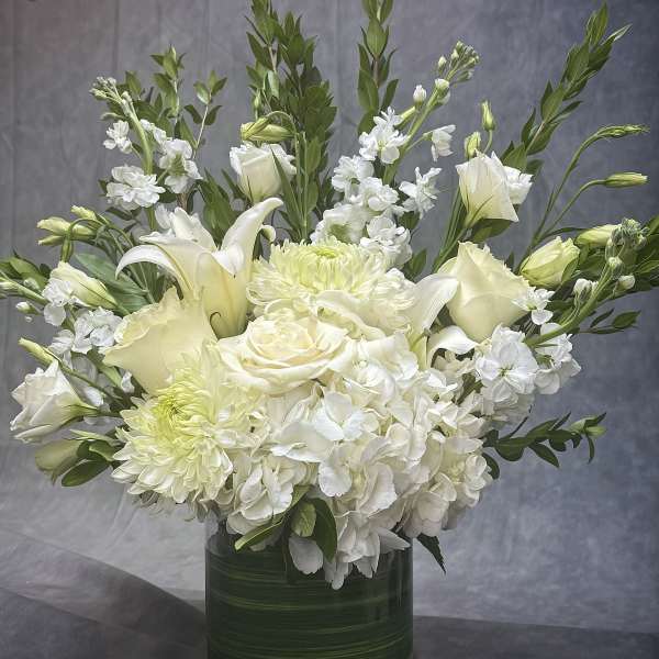 White floral arrangement in a green glass vase with lilies, roses, and hydrangeas
