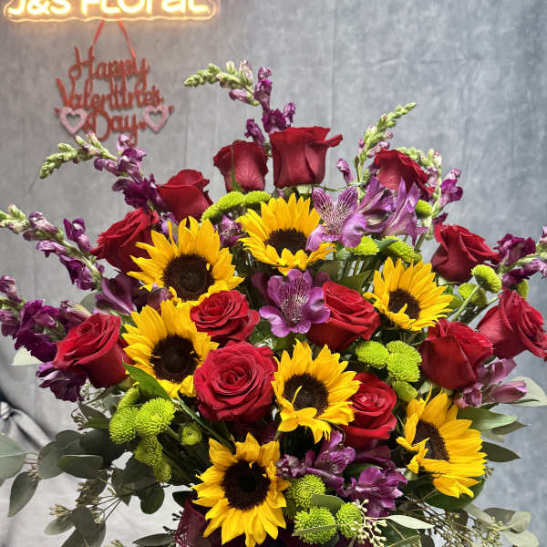 Bouquet of red roses, sunflowers, and purple flowers in a glass vase