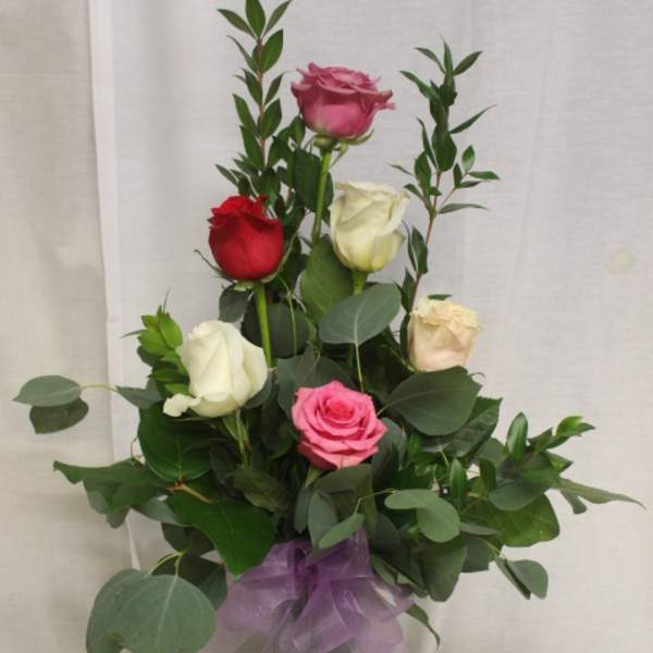 Bouquet of multicolored roses in a clear glass vase with a purple ribbon