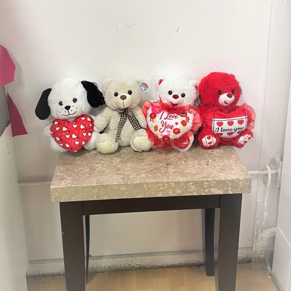 Four plush teddy bears holding heart pillows on a table