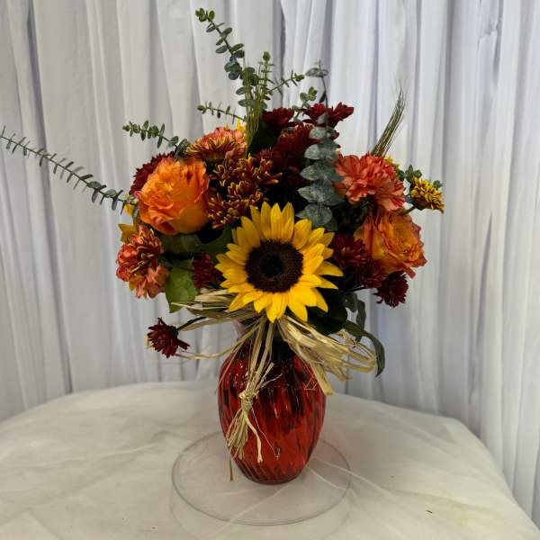 Bouquet of sunflowers, orange roses, and burgundy mums in a red vase