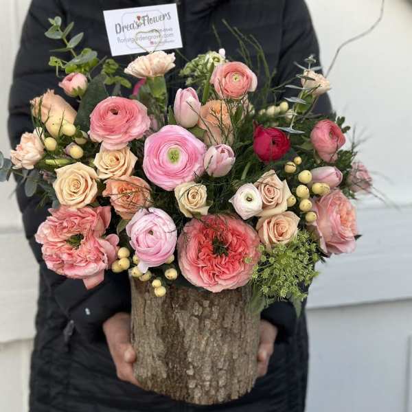 Mixed pink and peach flowers arranged in a rustic wood container