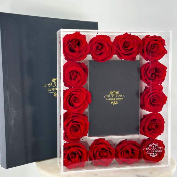 Red roses arranged in a clear box around a black gift box