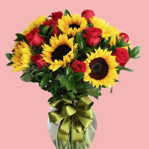 Bouquet of red roses and yellow sunflowers in a glass vase with a ribbon