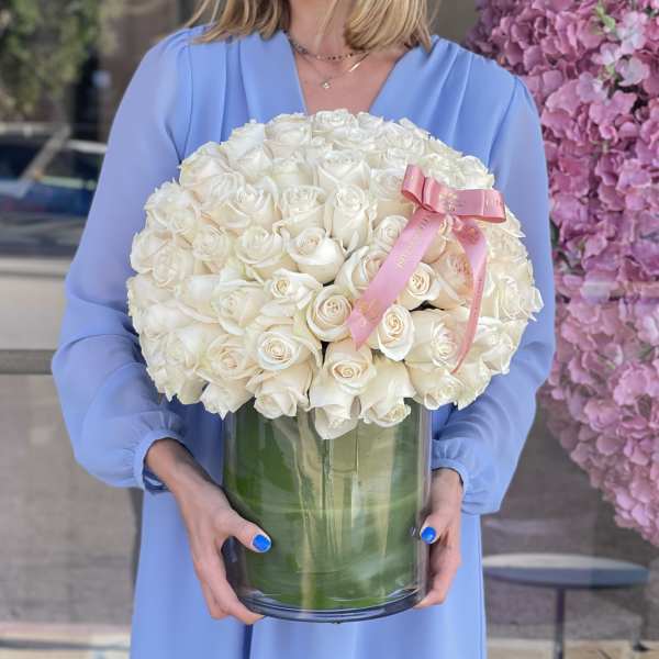 Large bouquet of white roses in a clear glass vase with a pink ribbon