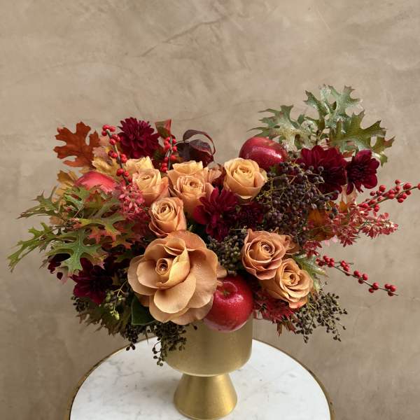 Peach roses and burgundy flowers in a gold vase with autumn leaves and berries