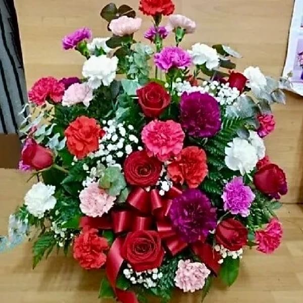 Mixed bouquet of red, pink, white, and purple flowers with a red ribbon