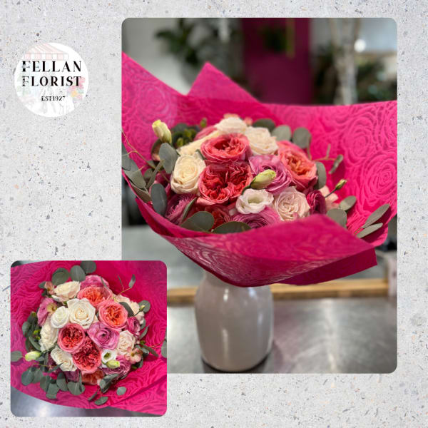 Hand-tied bouquet of pink, peach, and cream roses in bright magenta wrap, displayed in a white vase.