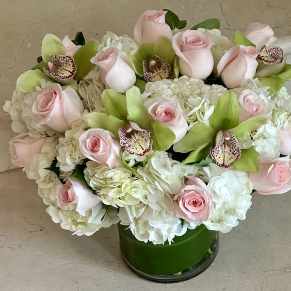 Pink roses and white hydrangeas with green orchids in a glass vase
