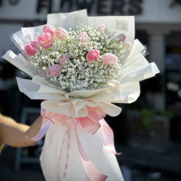 Pink tulip bouquet with baby's breath wrapped in white paper and ribbon