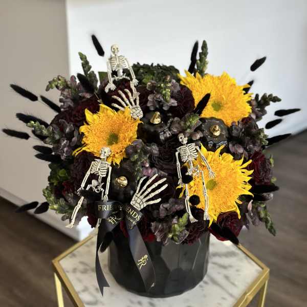 Black floral arrangement with yellow blooms and small skeleton decorations in a black vase