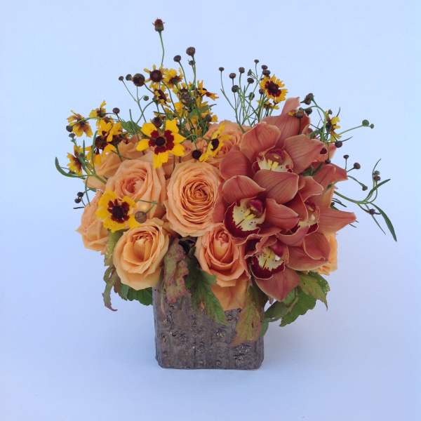 Peach roses and burgundy orchids in a square vase