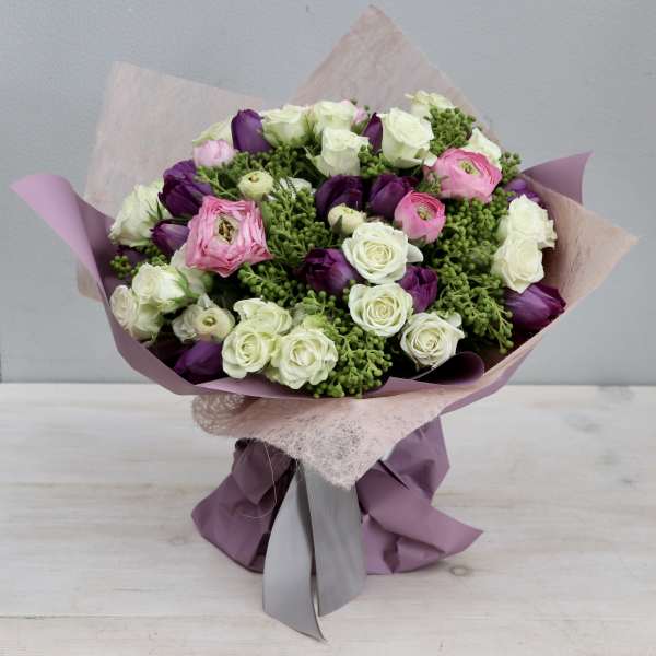 Hand-tied bouquet of white roses, purple tulips, pink ranunculus and green berries in mauve wrapping