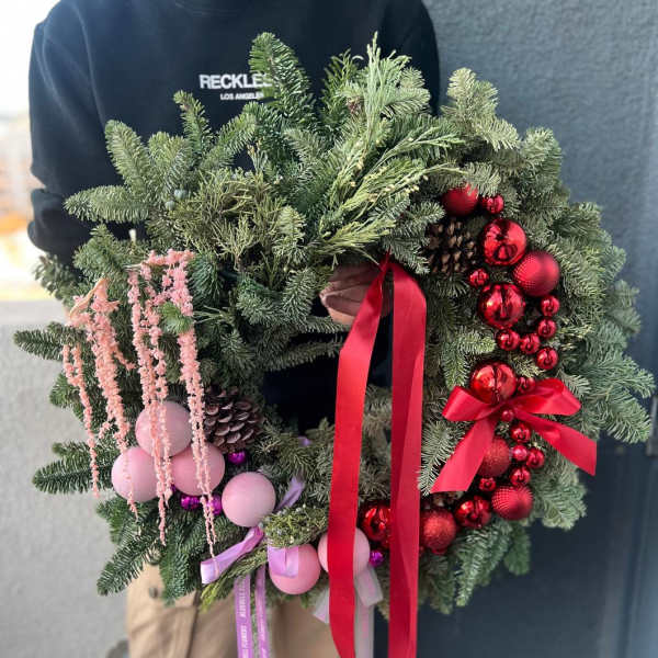 Holiday wreath with evergreen branches, red ornaments, and pink accents
