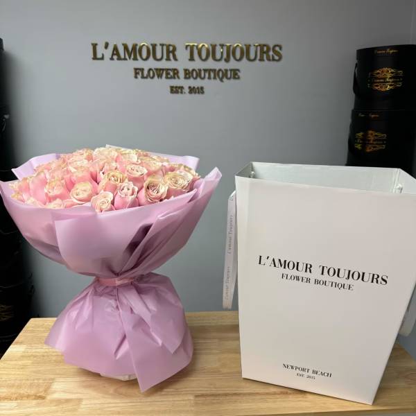 Bouquet of pale pink roses wrapped in lavender paper beside a white gift bag