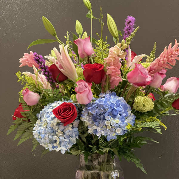 Mixed bouquet of roses, lilies, hydrangeas, and pink blooms in a glass vase