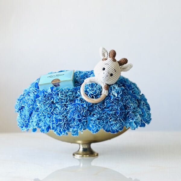 Blue floral arrangement in a gold bowl with a crocheted giraffe and small box