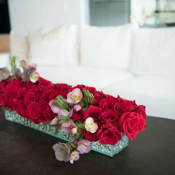 Long rectangular arrangement of red roses with pale pink flowers in a glass vase