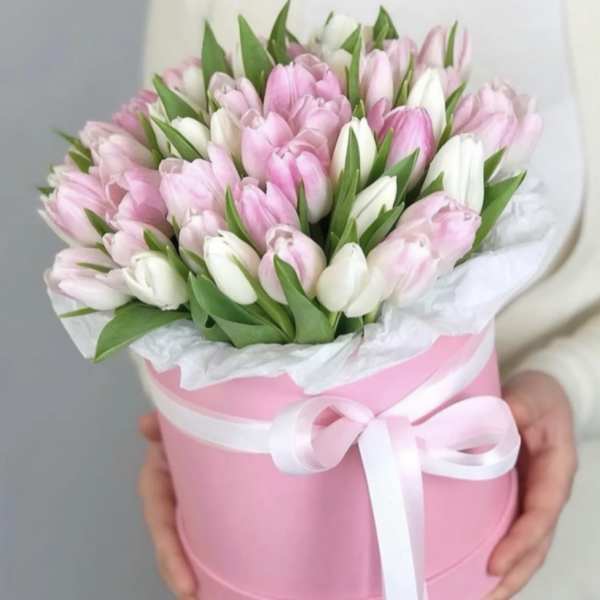 Pink and white tulips arranged in a pink hatbox with a ribbon
