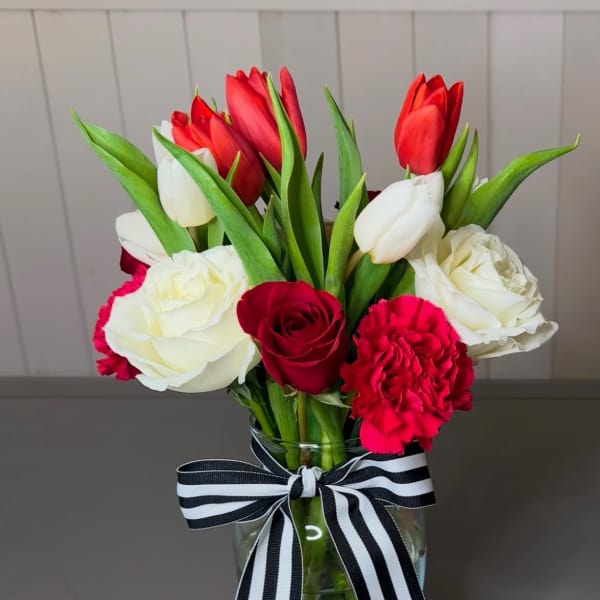 Bouquet of red and white tulips and roses in a glass vase with a striped ribbon
