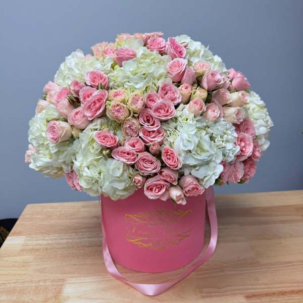 Pink roses and white hydrangeas in a pink hat box with ribbon