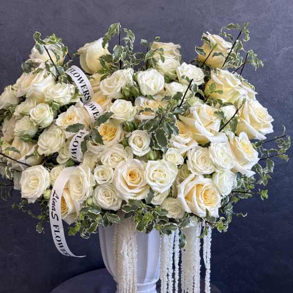 Cream rose arrangement in a white urn with trailing white accents