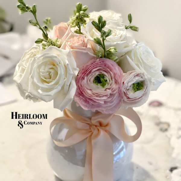 Pink and white roses with ranunculus in a white vase tied with a blush ribbon