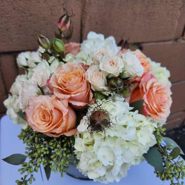 Low arrangement of peach roses, cream spray roses, and white hydrangeas in a round vase