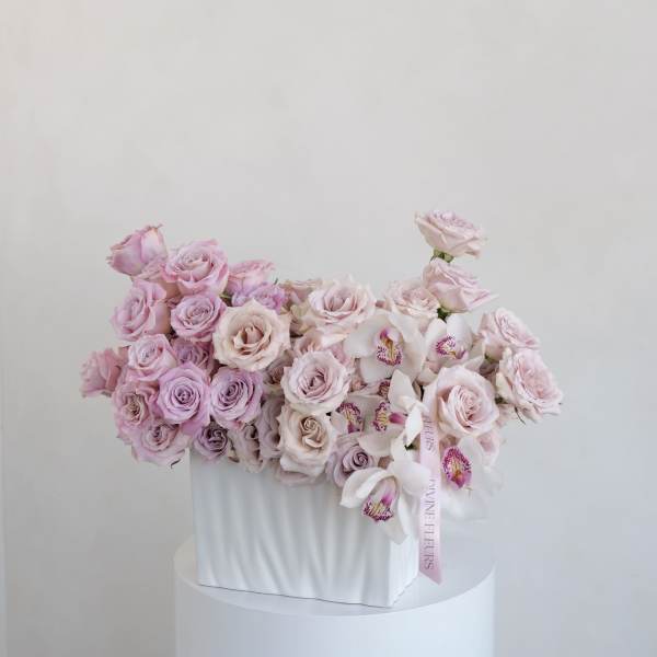 Pink roses and white orchids arranged in a white box
