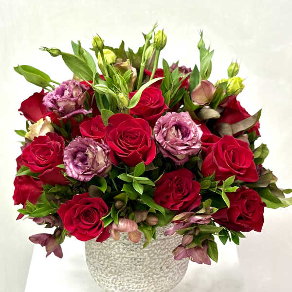 Red roses and pink lisianthus in a textured white vase