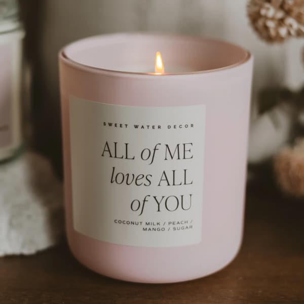Pink candle in a glass jar with a lit flame and printed label