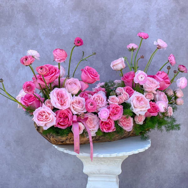 Pink roses and ranunculus arranged in a low basket on a pedestal