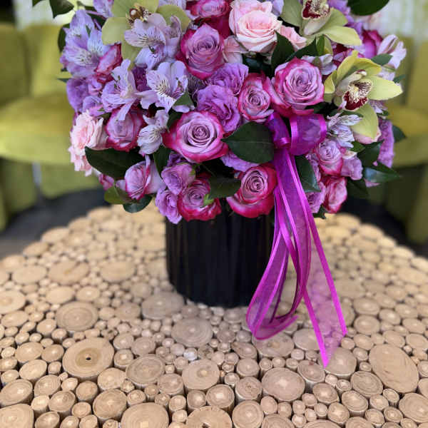 Pink and lavender bouquet of roses and orchids in a black vase with ribbon