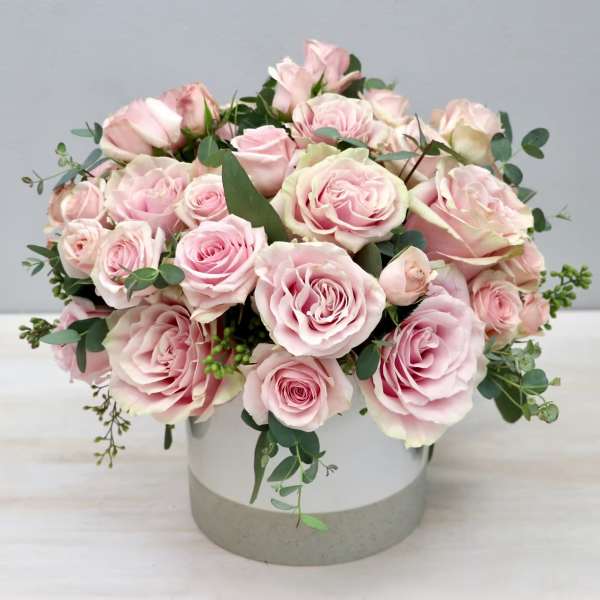 Pink roses arranged in a round white vase with eucalyptus accents