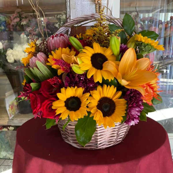 Wicker basket arrangement with yellow sunflowers, orange lilies, red roses and mixed blooms.