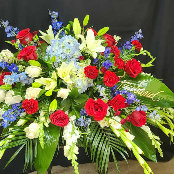 Large floral spray with red and white roses, lilies, and blue flowers