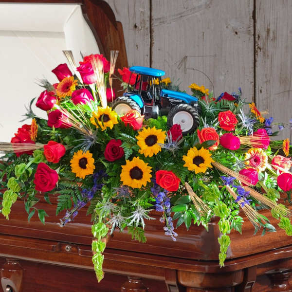 Colorful floral casket spray with a toy tractor centerpiece