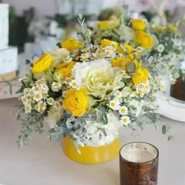 Yellow and white floral centerpiece in a low round container