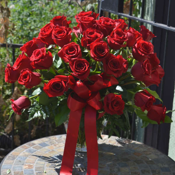 Large bouquet of red roses in a clear vase with a red ribbon bow on a mosaic table