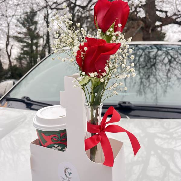 Two red roses in a small glass vase with baby's breath and a red ribbon