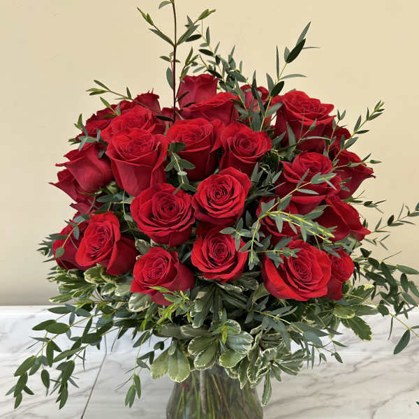 Red roses arranged in a clear glass vase with mixed greenery