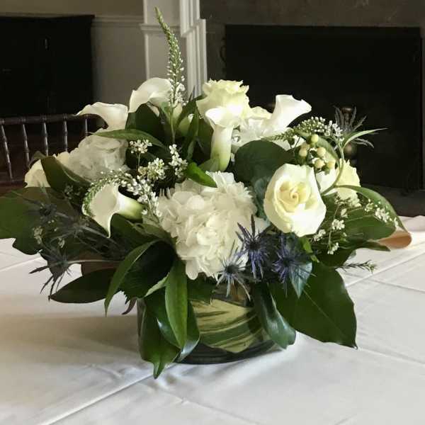 White floral arrangement with roses, calla lilies, and hydrangea in a glass vase