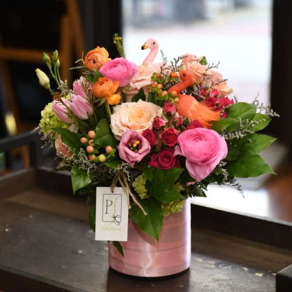 Mixed pink and orange flower arrangement with flamingo decorations in a pink vase.