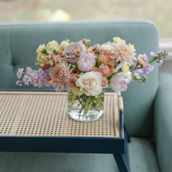 Pastel mixed flower bouquet in a clear glass vase on a tray table