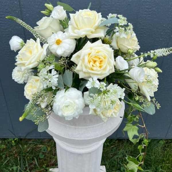 Ivory and white rose arrangement with accent blooms in a white pedestal urn
