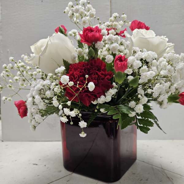 Red and white carnations with baby’s breath in a dark glass vase