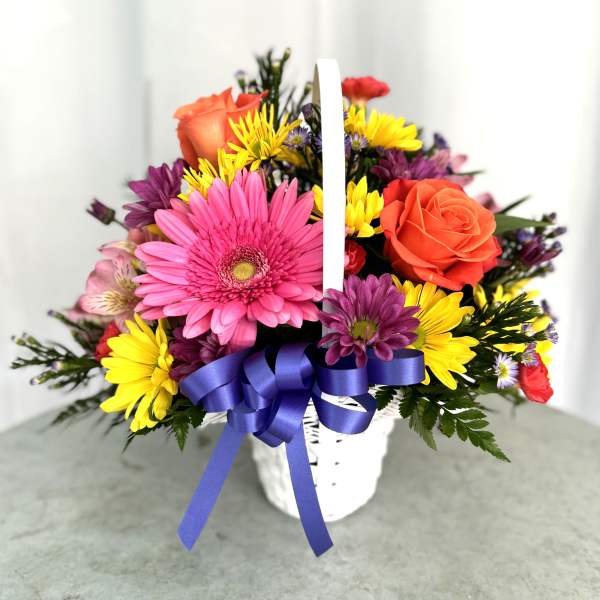 Mixed bouquet in a white basket with a purple ribbon