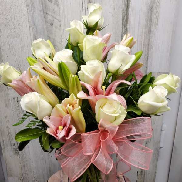 Bouquet of white roses and pink lilies in a glass vase with a pink ribbon